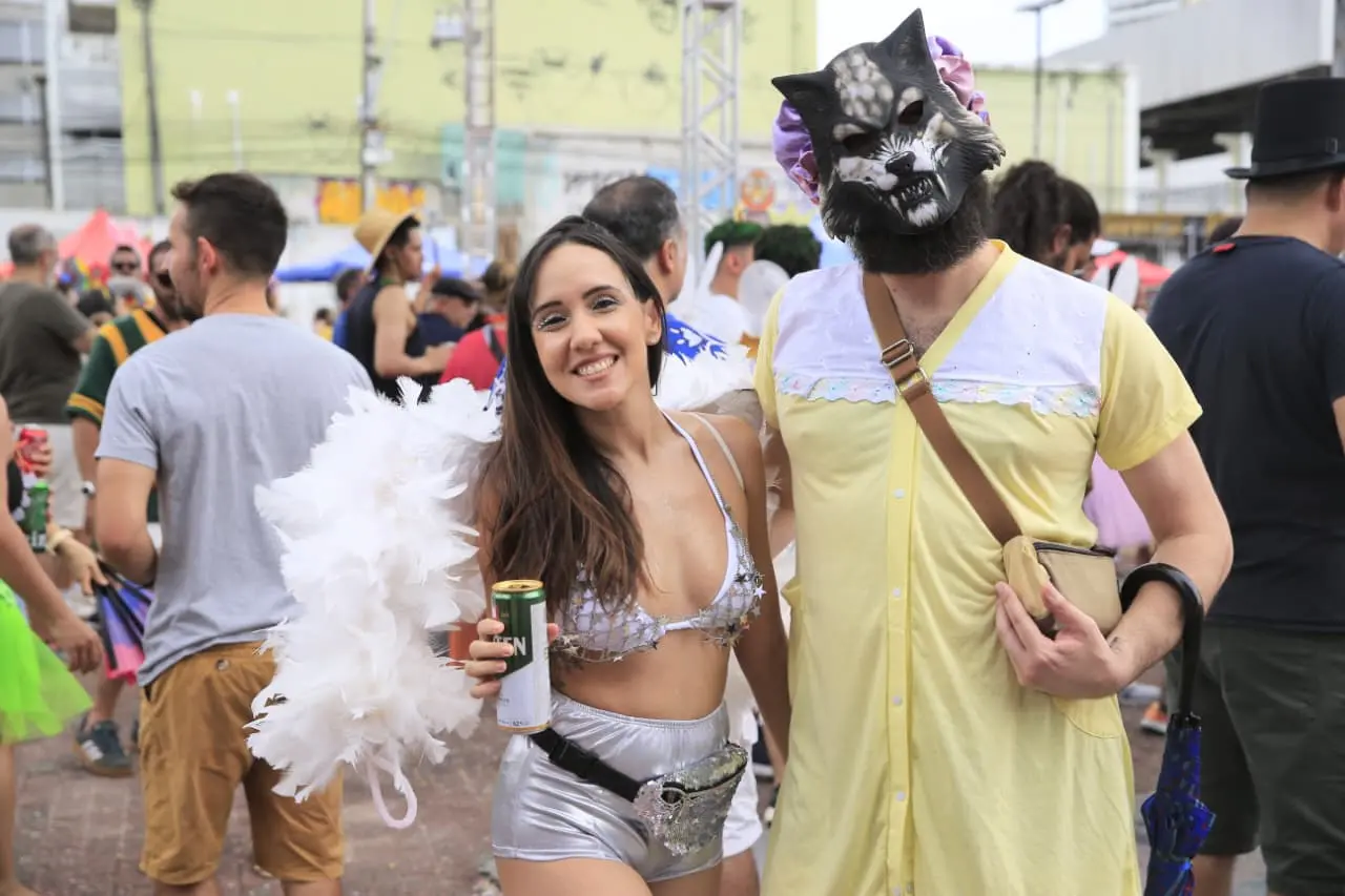 Folião vestido de lobo mau vestido de vovozinha ao lado de garota vestida de anjo.