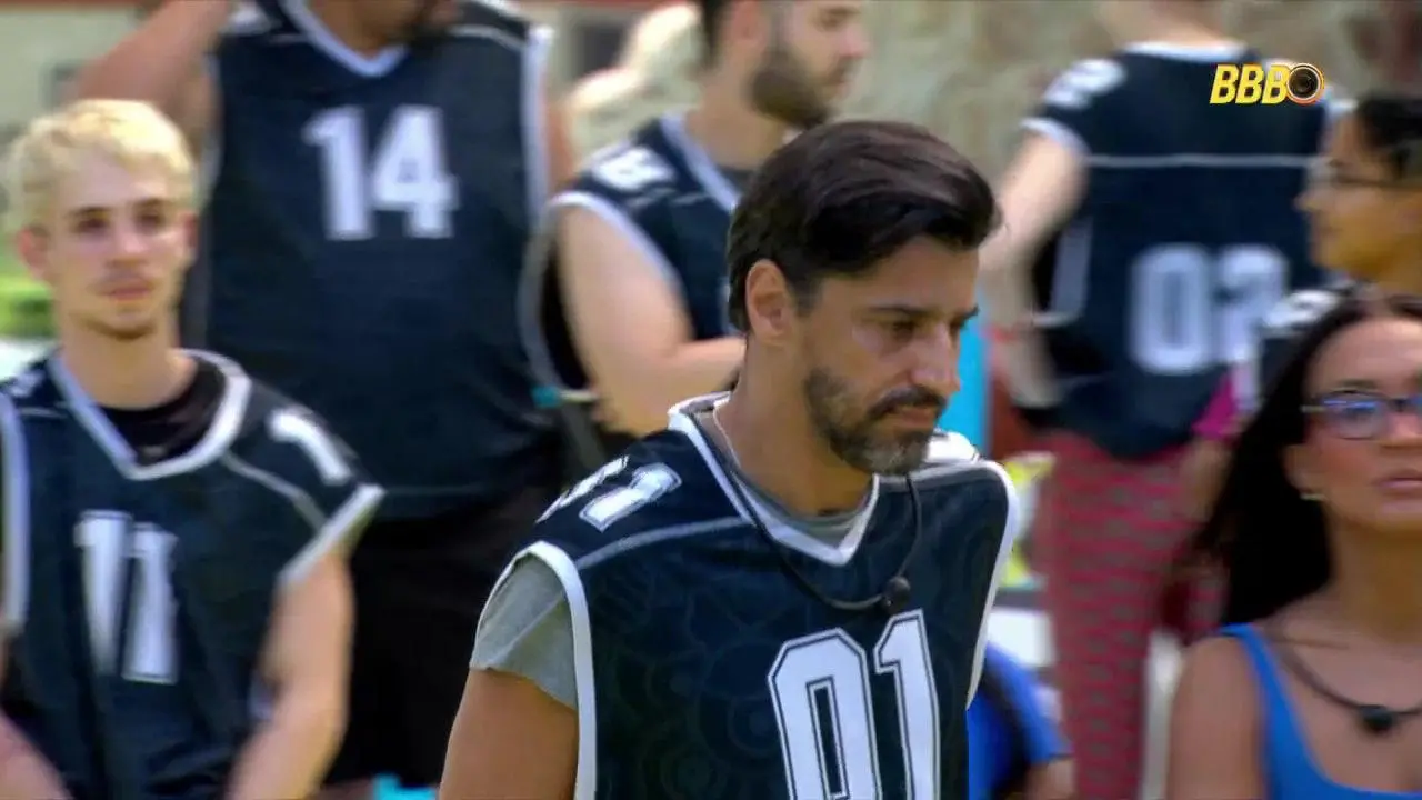 Alberto Cowboy no BBB 26 com colete preto, cabeça baixa e expressão de descontentamento no rosto.