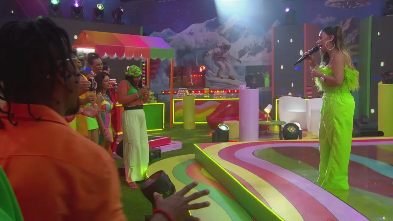 Simone Mendes comandou a festa. Na imagem, ela está sobre um pequeno palco segurando o microfone e cantando. Na frente dela, alguns participantes do BBB 26, entre eles Boneco.