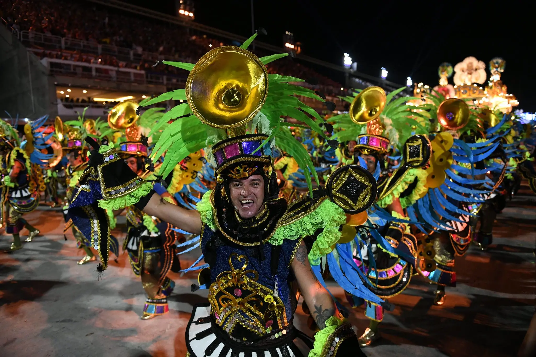 Passista sorri e abre os braços durante o desfile do ano passado. Ao fundo, outros passistas vestidos iguais a ele.