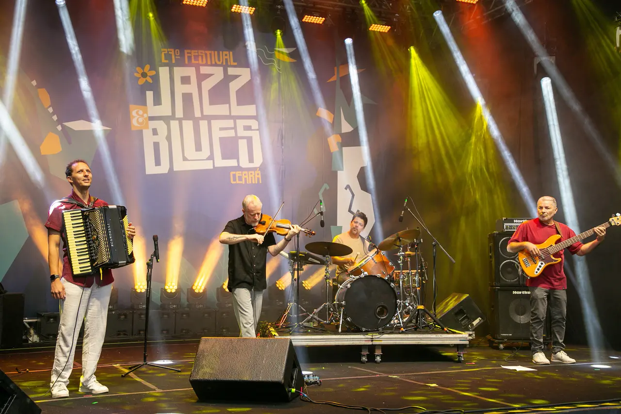 Imgem de 4 homens brancos em um palco, no show de Nicolas Krassik. Um deles toca um sanfone, outro um violino, um está na bateria e o outro com um baixo.