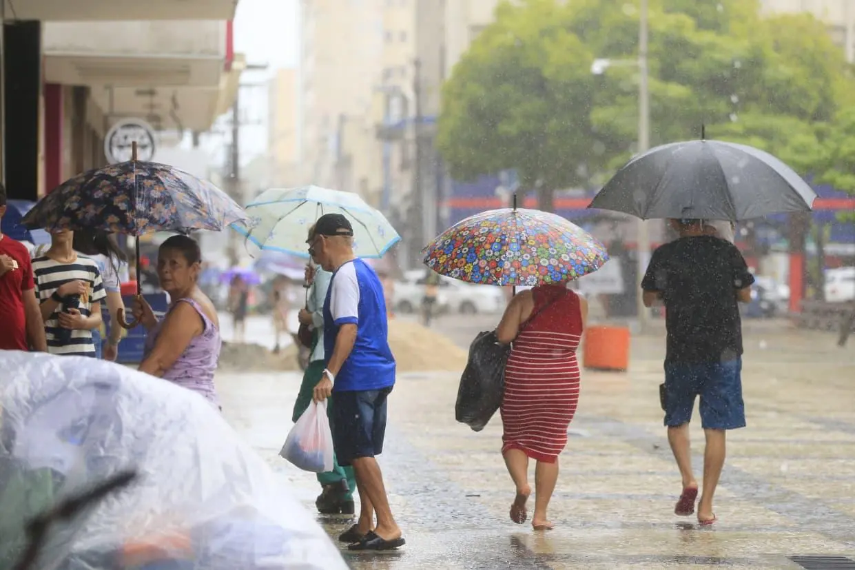 Pessoas andando com guarda-chuvas em praça.