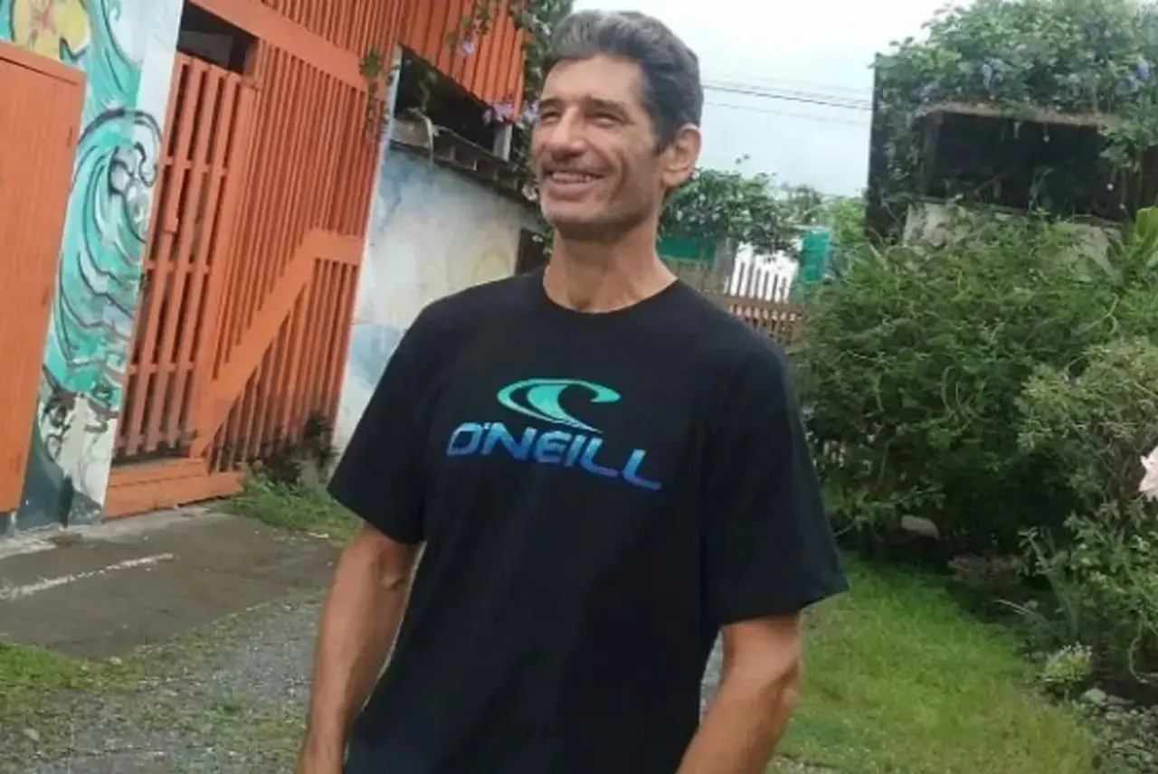 Surfista Kurt Van Dyke sorridente em frente a um portão de madeira. Atleta foi encontrado morto em sua casa na Costa Rica.