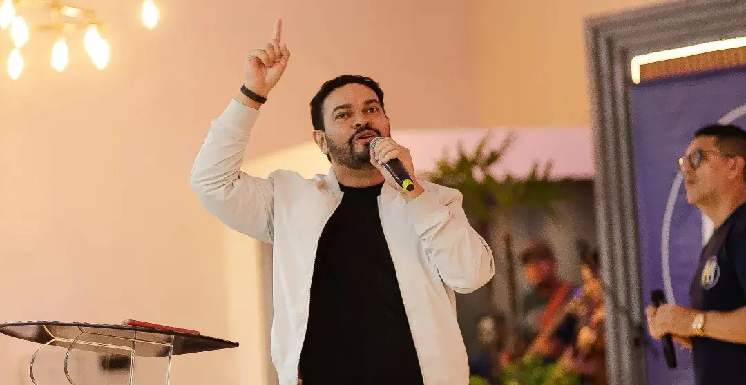 Fernando Grandêz durante apresentação musical. Ele aponta para cima com o dedo indicador e segura um microfone.