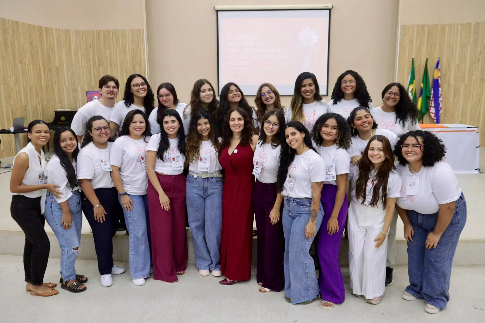 Imagem mostra grupo de mulheres usando camista branca em um espaço parecido com um auditório.
