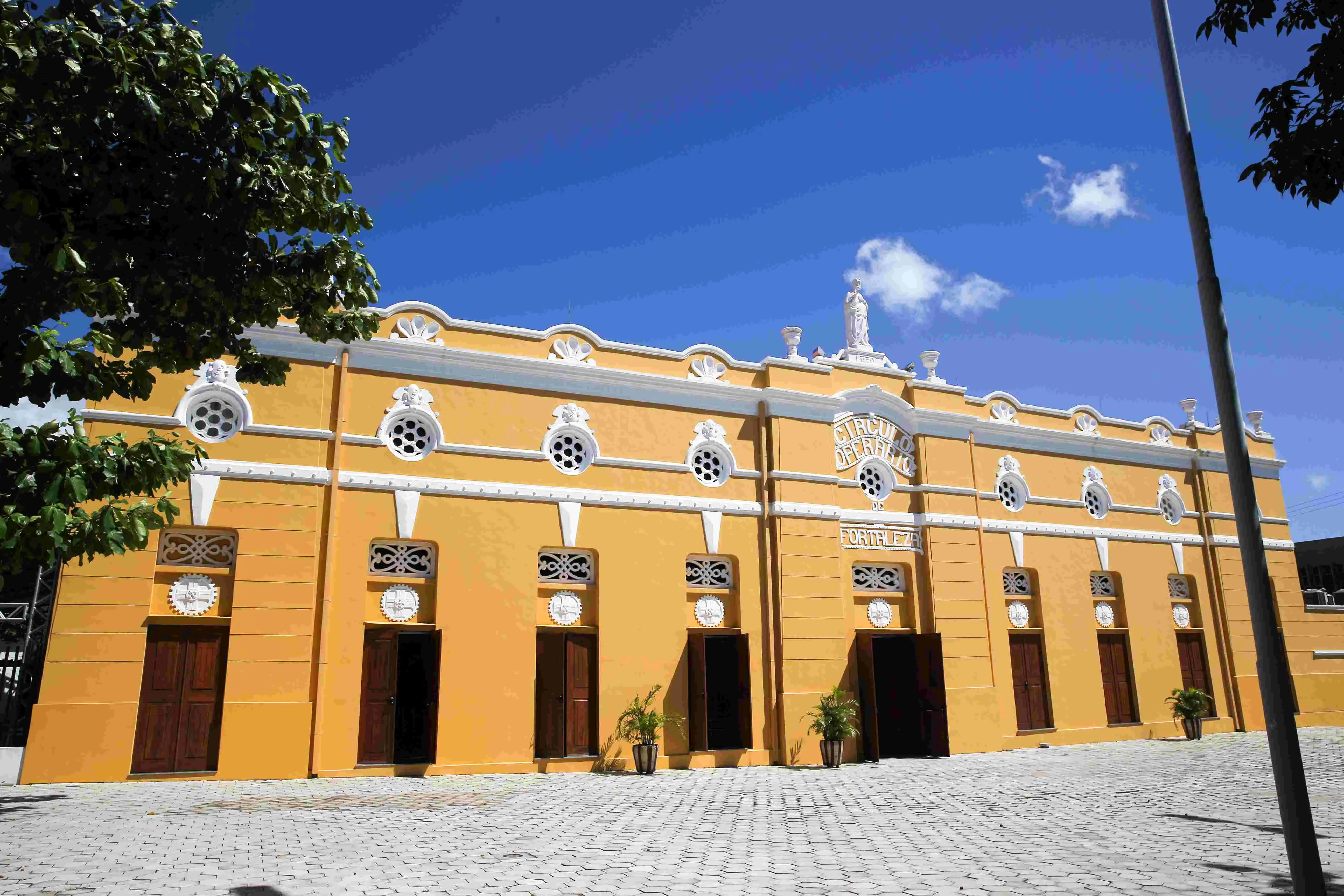 Edifício histórico do Teatro São José em Fortaleza, de fachada amarela vibrante com detalhes brancos ornamentados e portas de madeira, sob um céu azul claro.