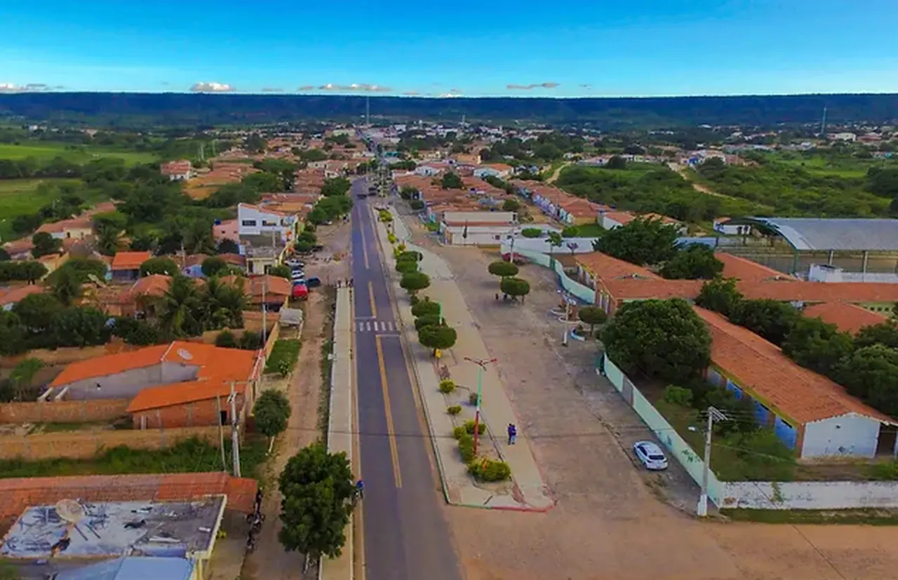 Imagem aérea mostra principal via do município de Salitre, com um canteiro no meio e baixas edificações na volta. Ao fundo é possível avistar a formação do relevo chamada de Chapada do Araripe.