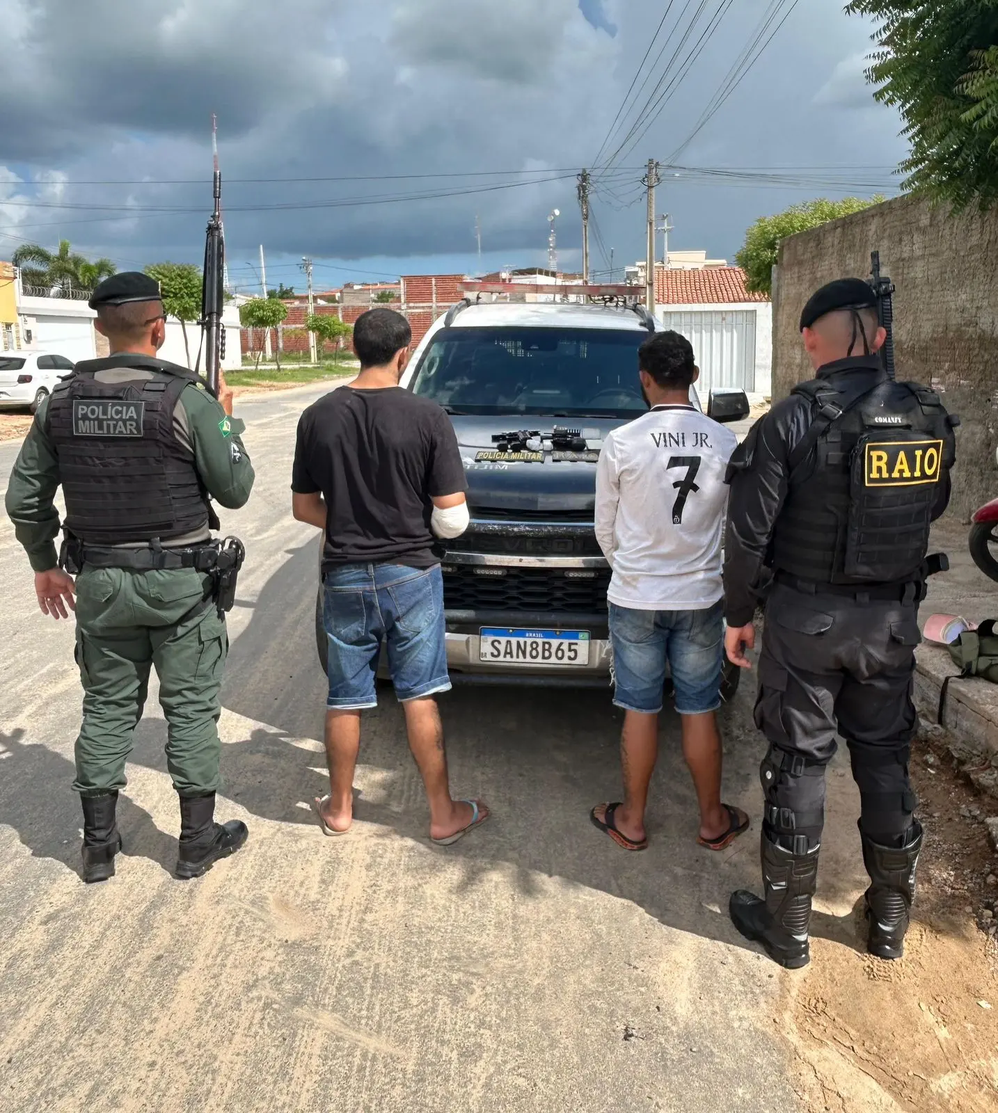 Imagem mostra dois policiais militares nas laterais e no centro dois homens de costas suspeitos de um homicídio em Orós.