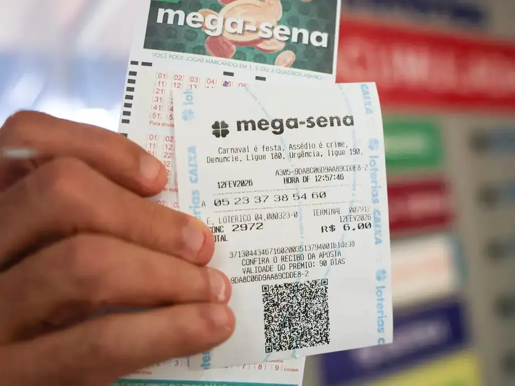 Dedos de um homem segurando papel da aposto na mega-sena.