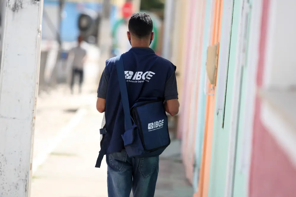Profissional do IBGE de costas caminhando em calçada.