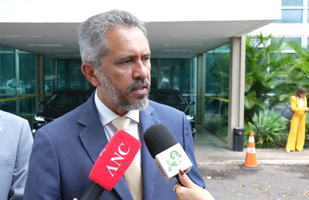 Elmano de Freitas posicionado diante da imprensa concede entrevista. Ele olha para a lateral e, diante dele, há dois microfones, um da TV Verdes Mares e outro da ANC.