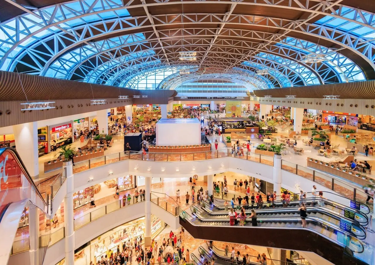 Três andares do shopping riomar fortaleza vistos de cima, mostrando parte da praça de alimentação, escada rolante e lojas.