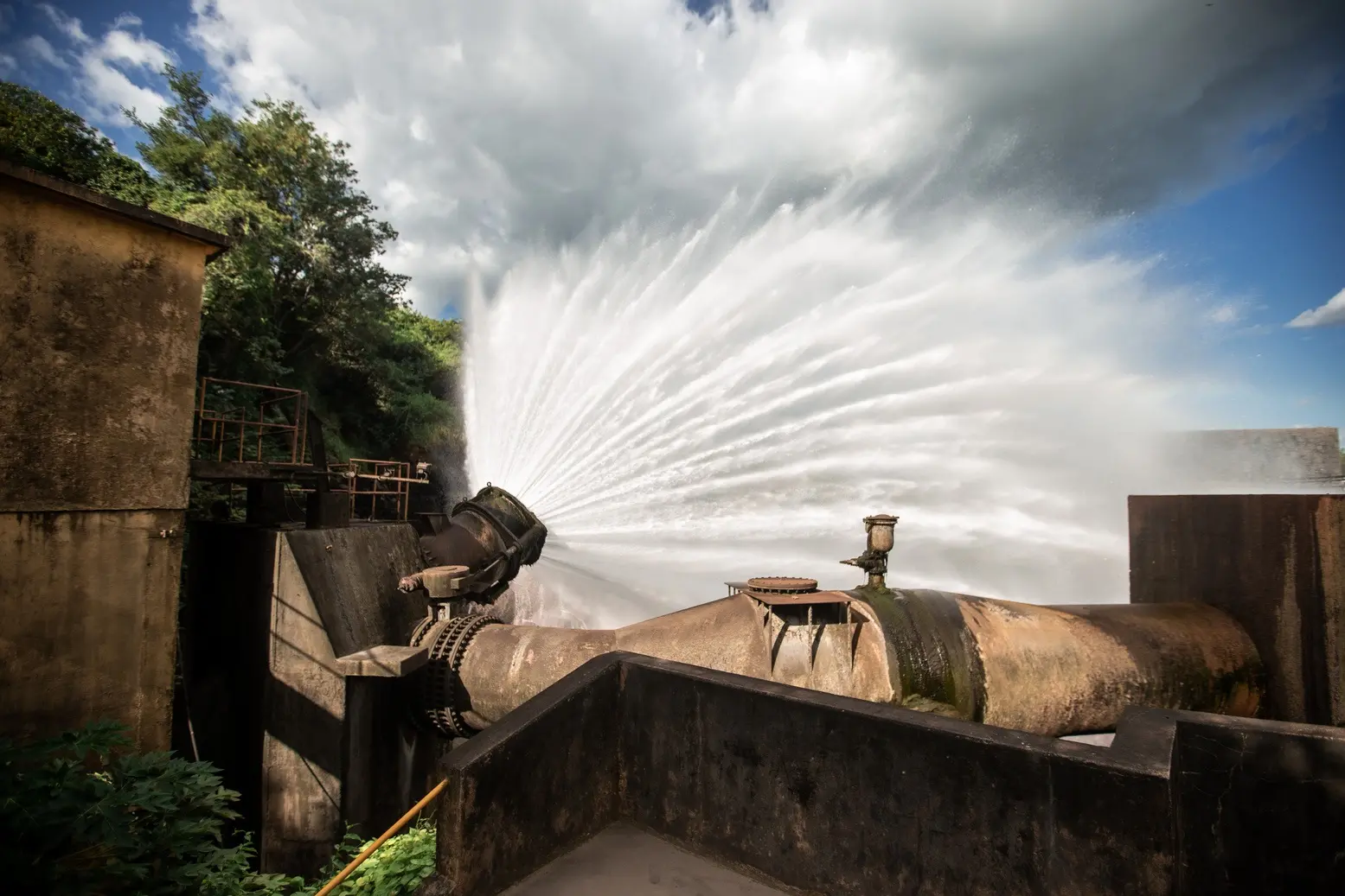 Jato de água potente em formato de véu sendo liberado de um tubo industrial robusto na barragem do açude Orós, no Ceará.