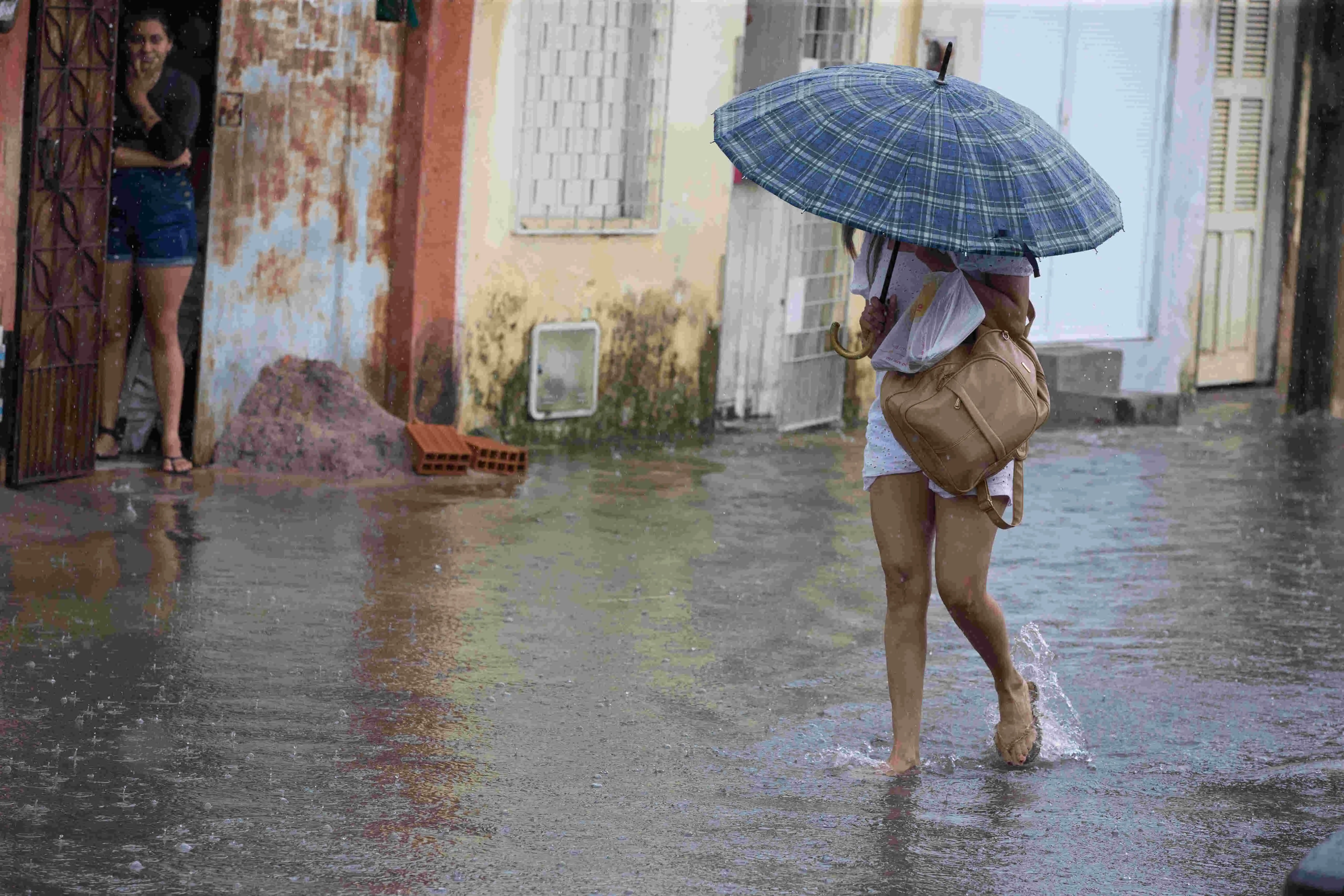 Mulher em alagamento segurando guarda-chuva e uma bolsa em um dia chuvoso.