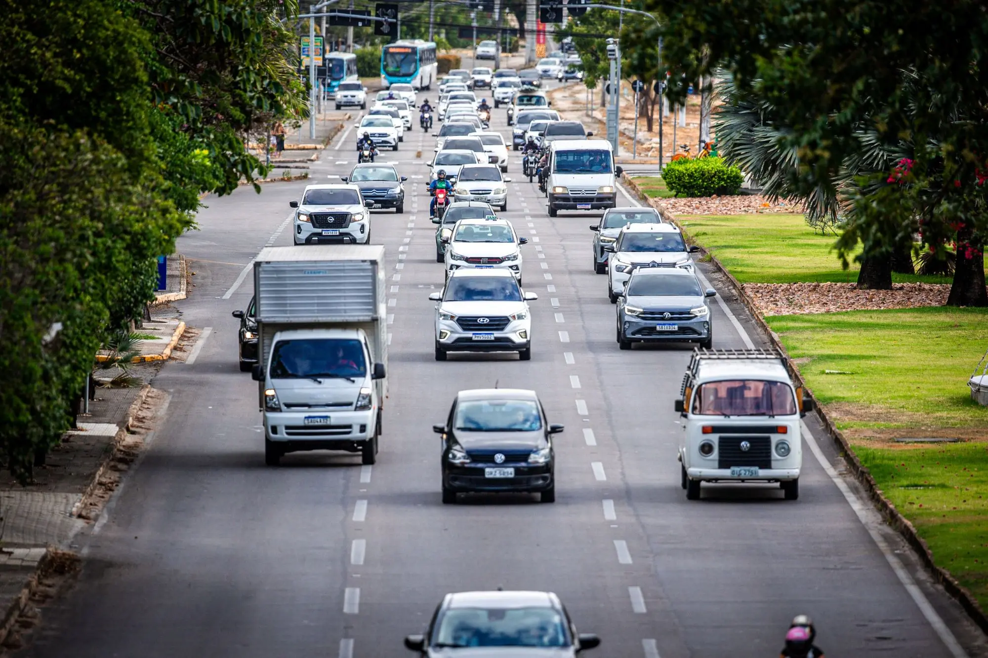 Trânsito congestionado na cidade com filas de carros e transporte público, durante o pôr do sol, refletindo o movimento intenso do deslocamento urbano.