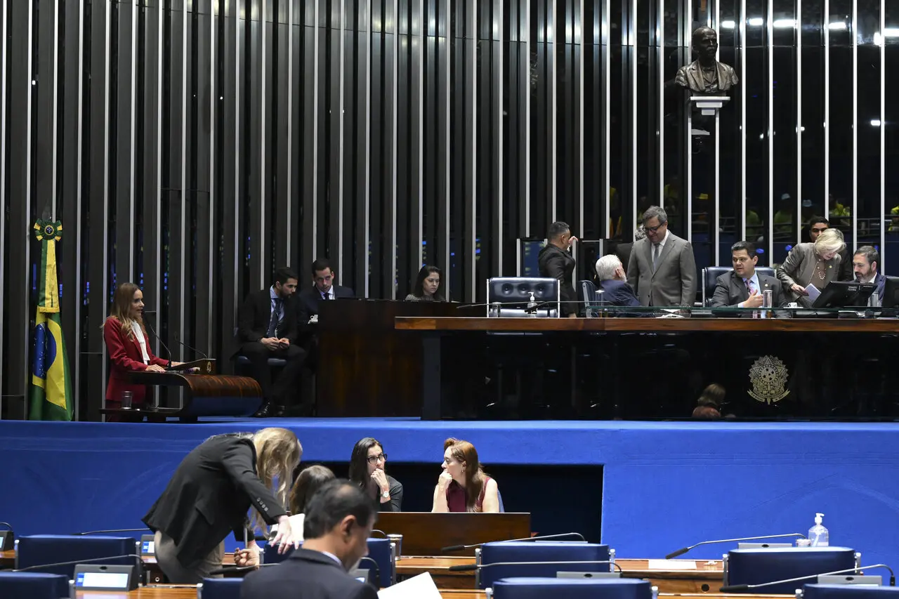 Imagem interna do Senado com mesa central e deputados ao redor.