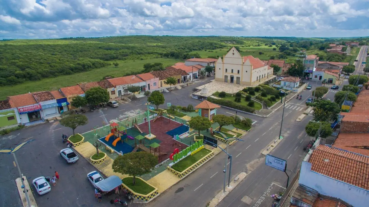 Vista aérea de uma cidade pequena, em que a igreja e uma praça estão em evidência, em meio a uma grande área verde.