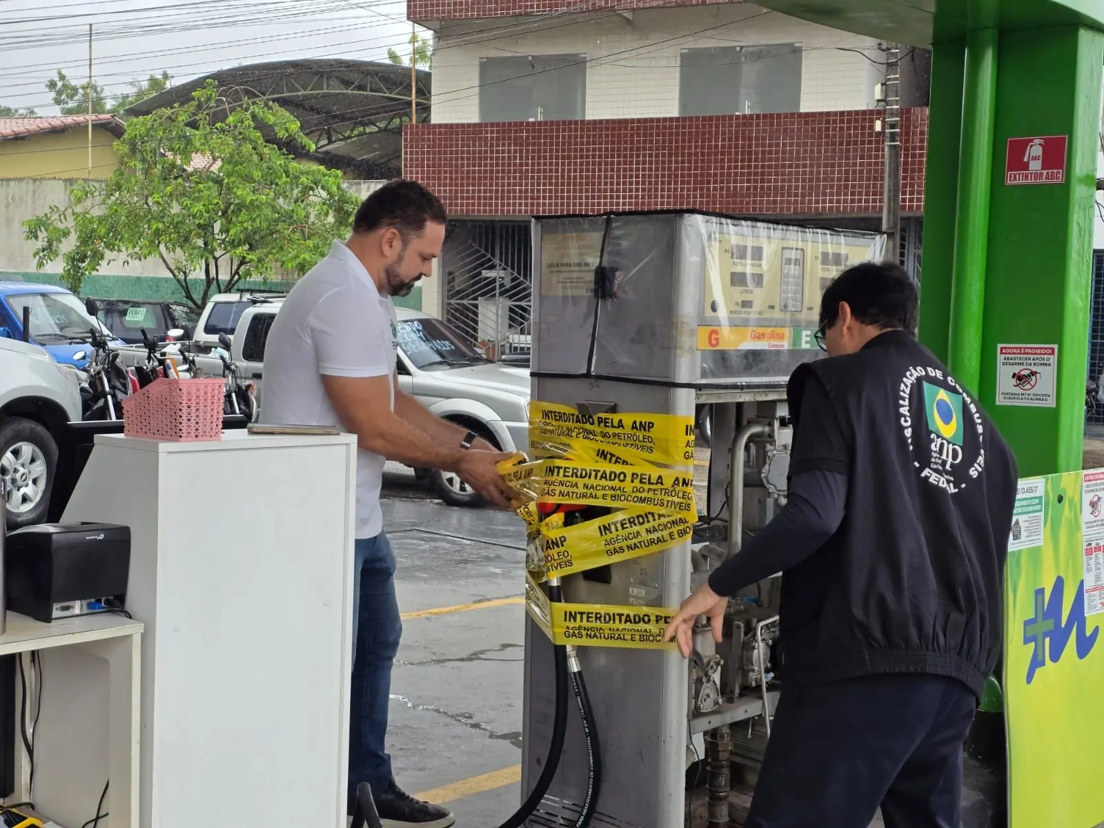 Imagem mostra dois servidores do Procon lacrando uma bomba de combustíveis.