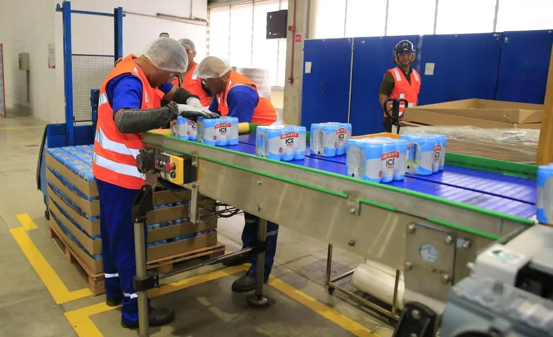 Homens trabalhando em ambiente de fábrica em esteria de latas de Smirnoff Ice.