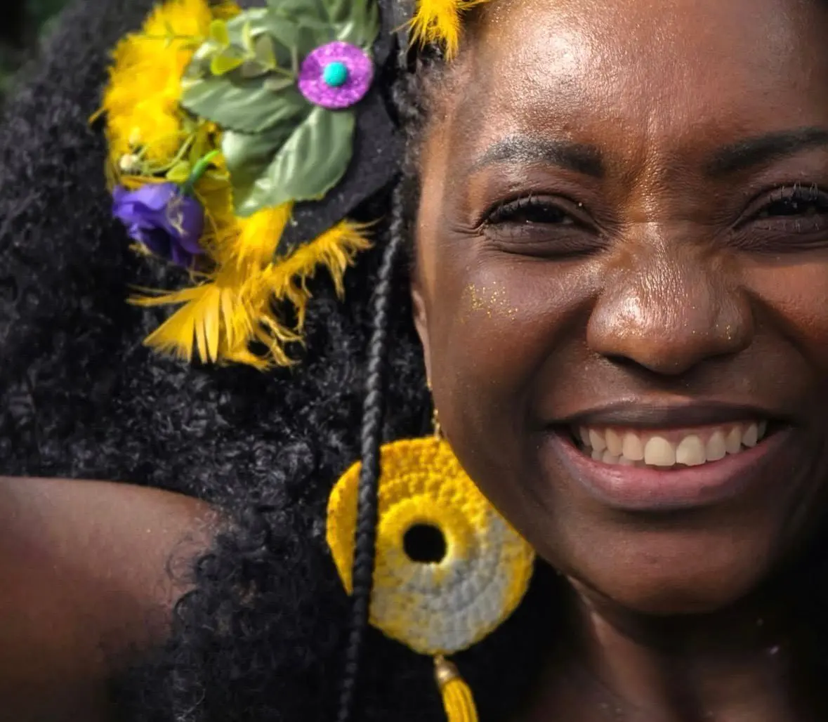 Adriana Araújo era uma mulher jovem, negra, de cabelos crepos pretos. Na foto, ela está usando brincos grandes amarelos, redondos, e enfeites no cabelo na mesma cor. Está sorrindo.