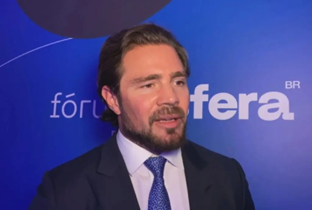 Daniel Vorcaro falando em evento com fundo azul que tem a palavra 'fórum' e 'BR', possivelmente em um contexto de debate ou apresentação.