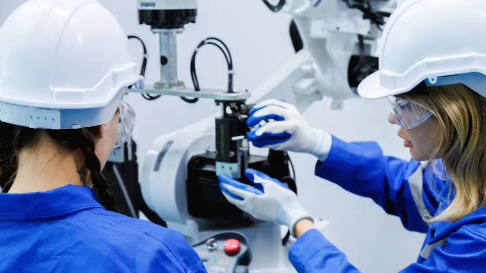 foto de duas mulheres jovens operando máquina. Elas usam equipamento de proteção na cabeça e luvas.