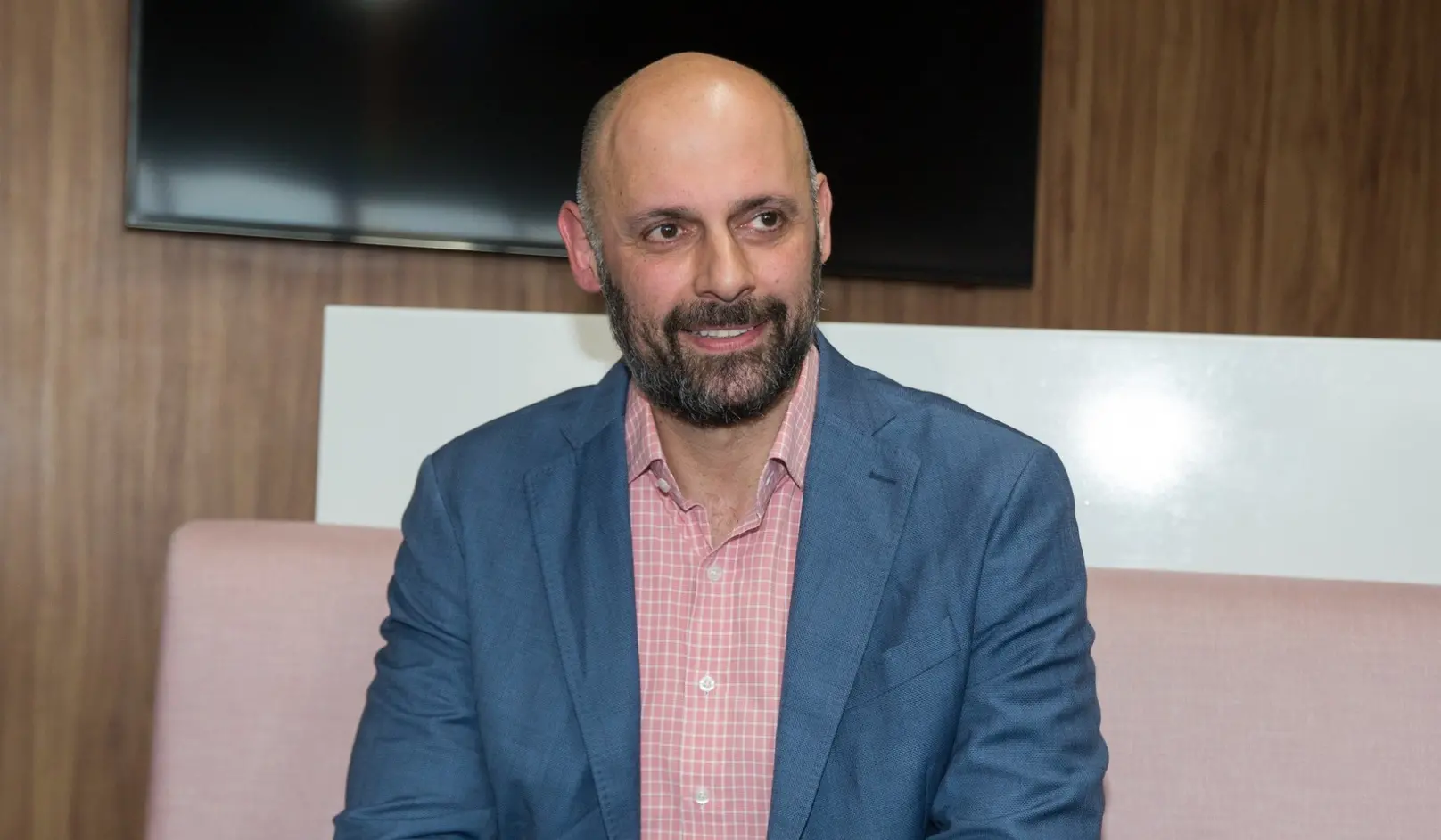 Homem de camisa rosa e blazer azul, conversando.