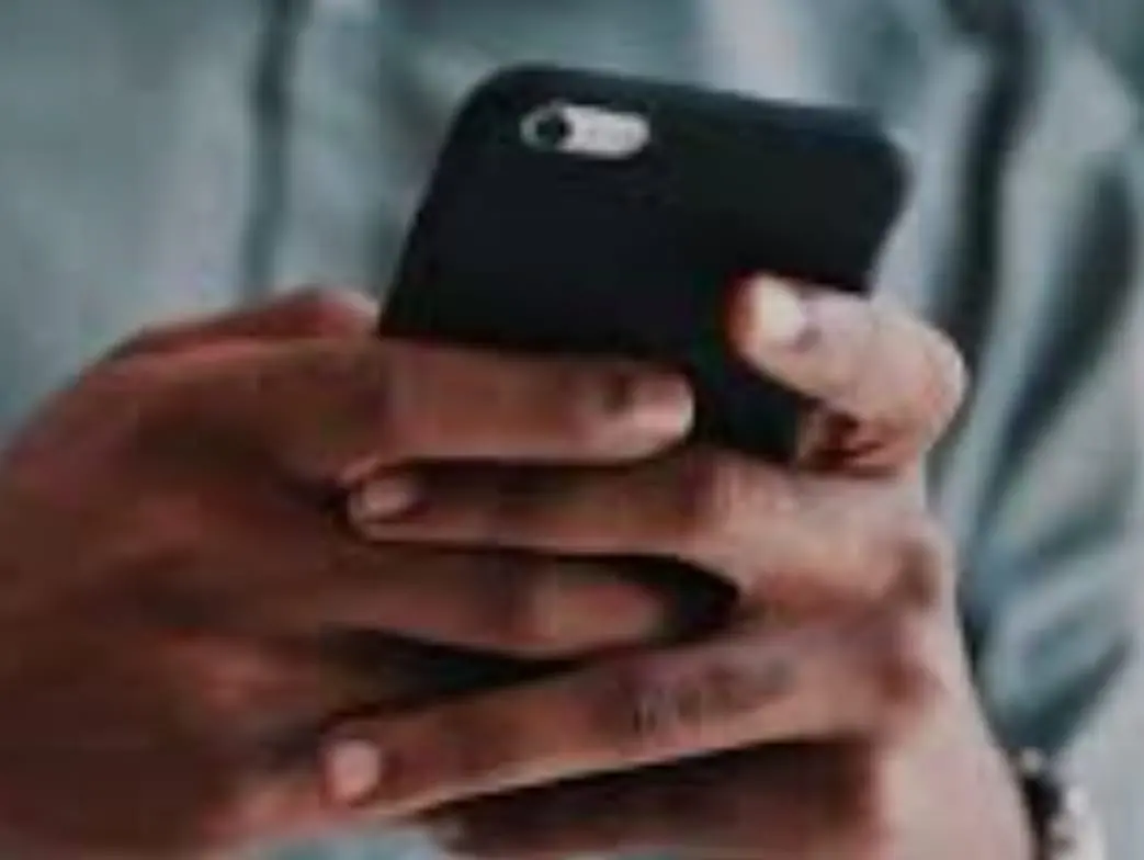 Pessoa segura um celular de capa preta com as duas mãos enquanto digita.