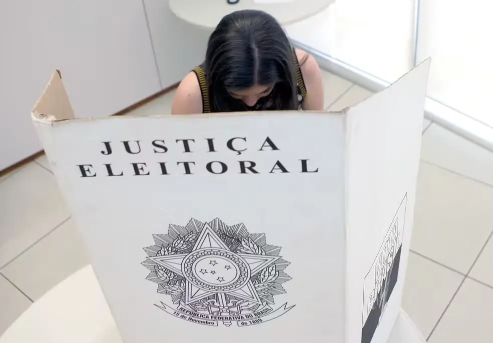 Eleitora vota em cabine de papelão da Justiça Eleitoral durante processo de votação.