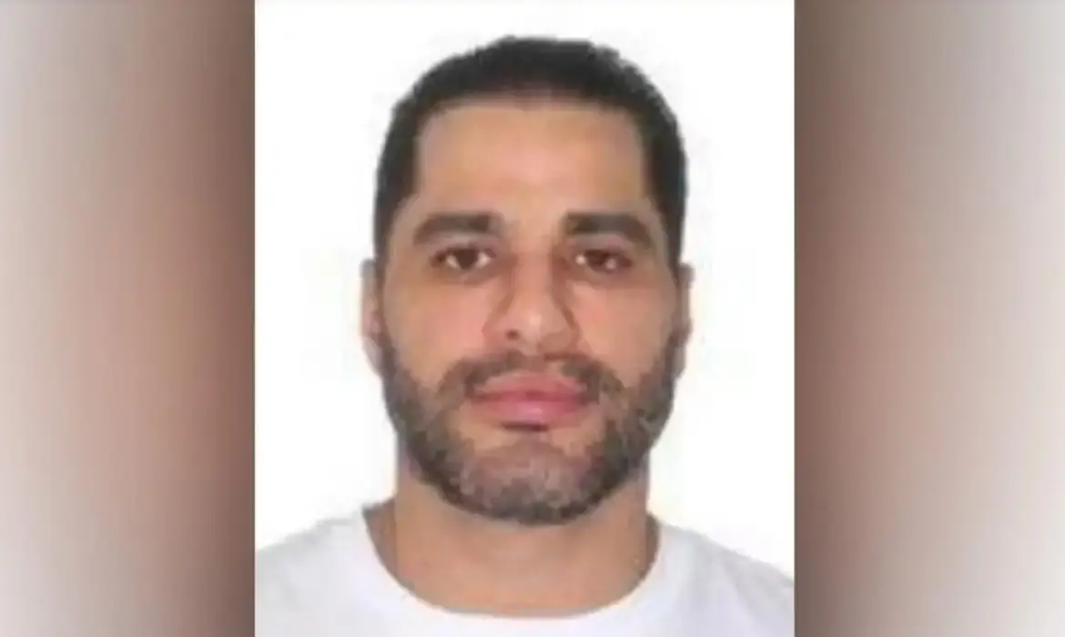 Na imagem Sicário esta em uma foto 3x4 usando uma camisa branca.