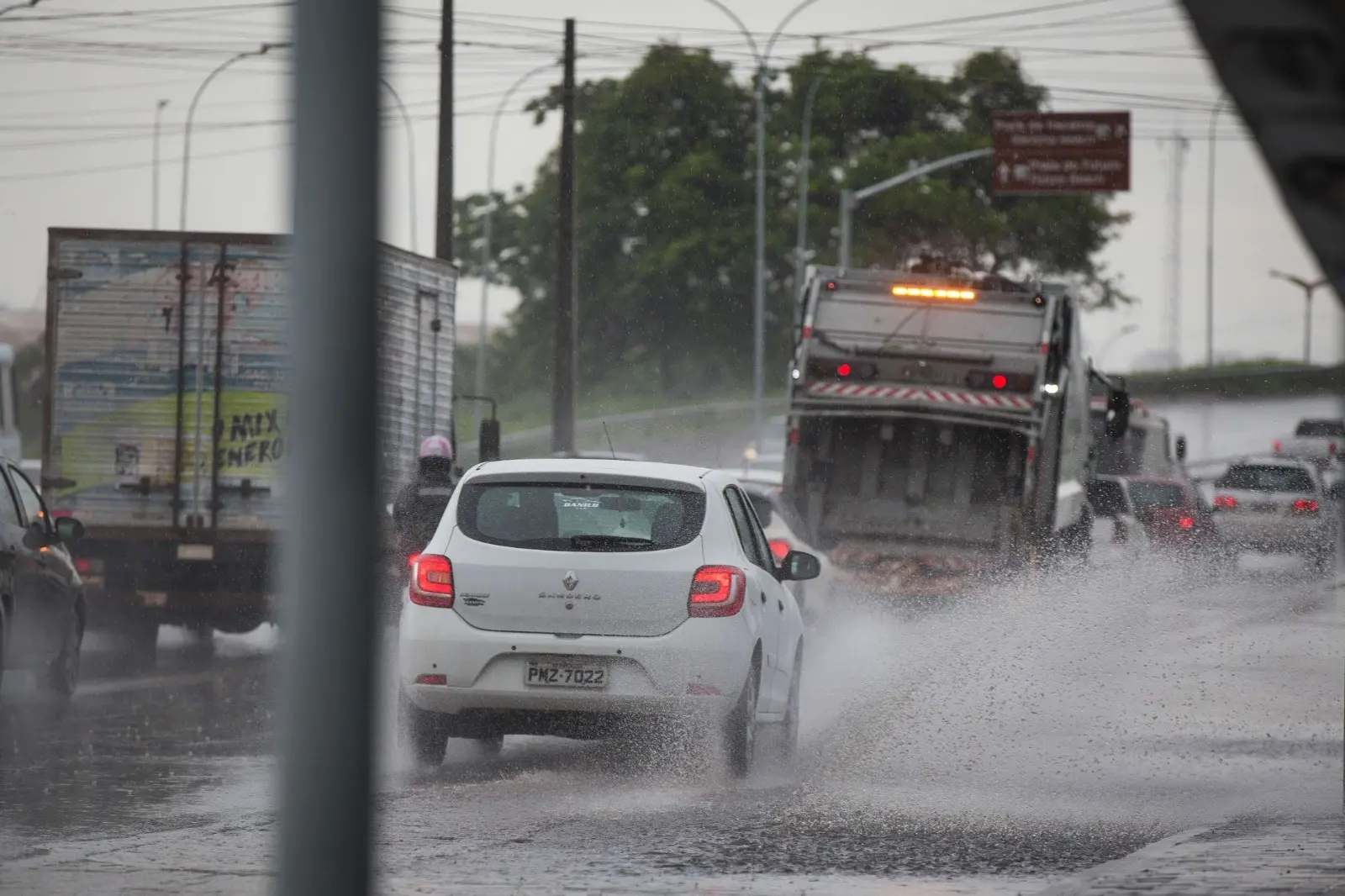 Foto de carros passando por área com pontos de alagamento na Avenida Alberto Craveiro, em Fortaleza.