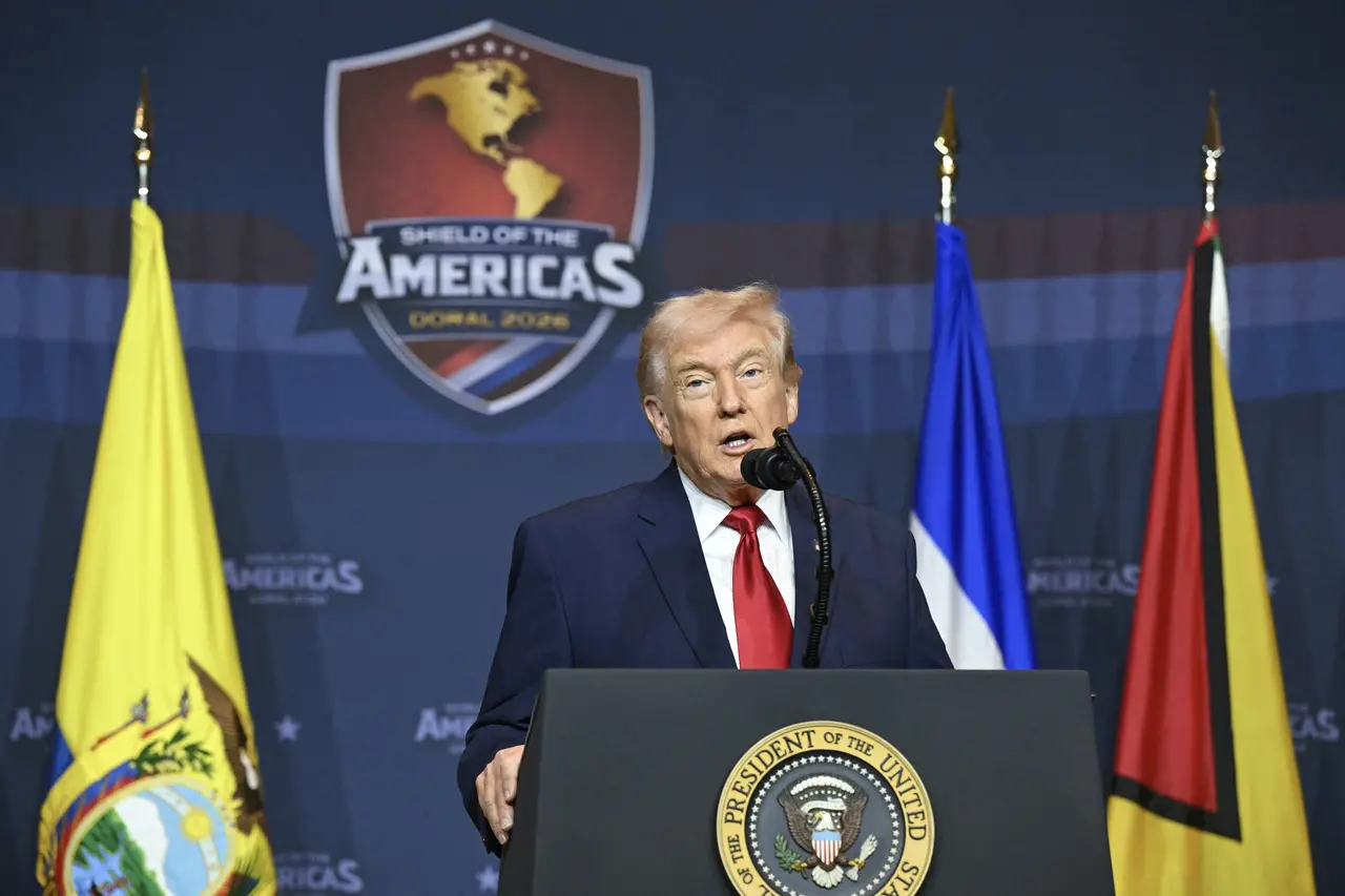 Donald Trump discursa em um púlpito com o selo presidencial dos Estados Unidos, posicionado entre bandeiras nacionais sob um fundo azul. Atrás dele, um escudo exibe o mapa das Américas com o texto 