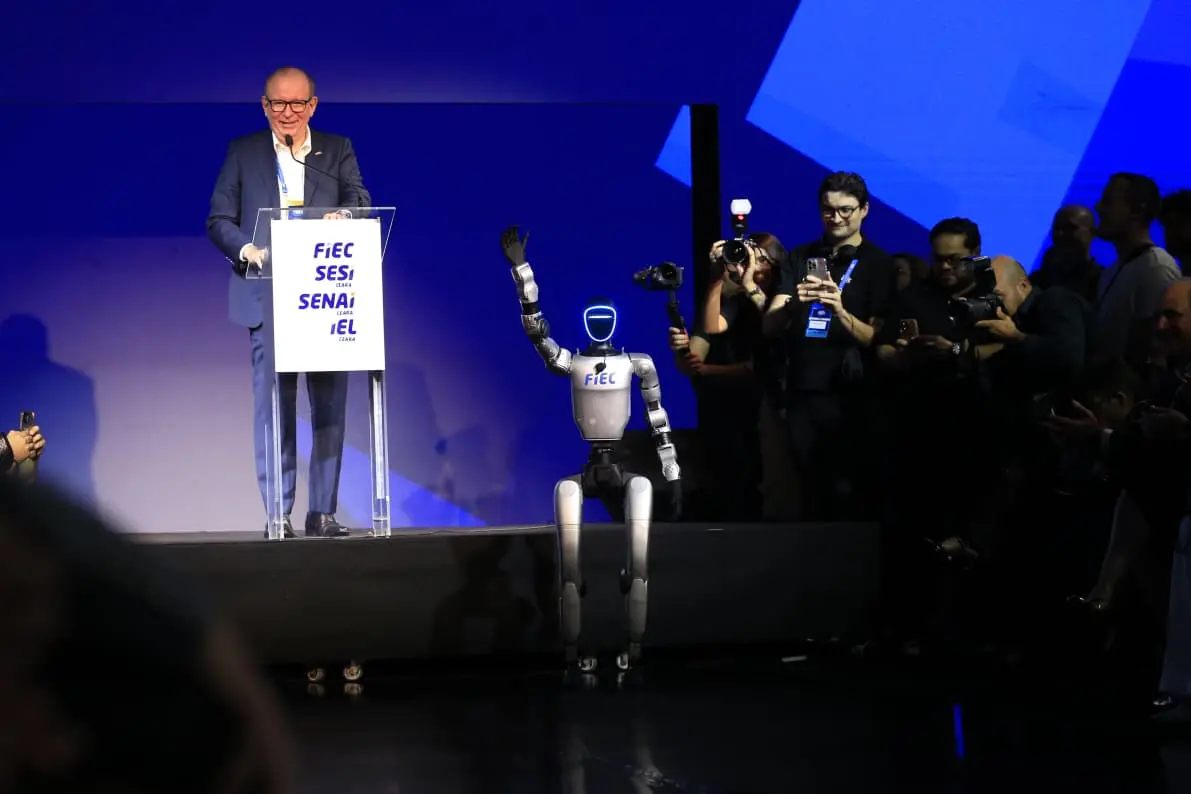 Presidente da Fiec em púlpito no palco e um robô sentado, com o braço levantado.