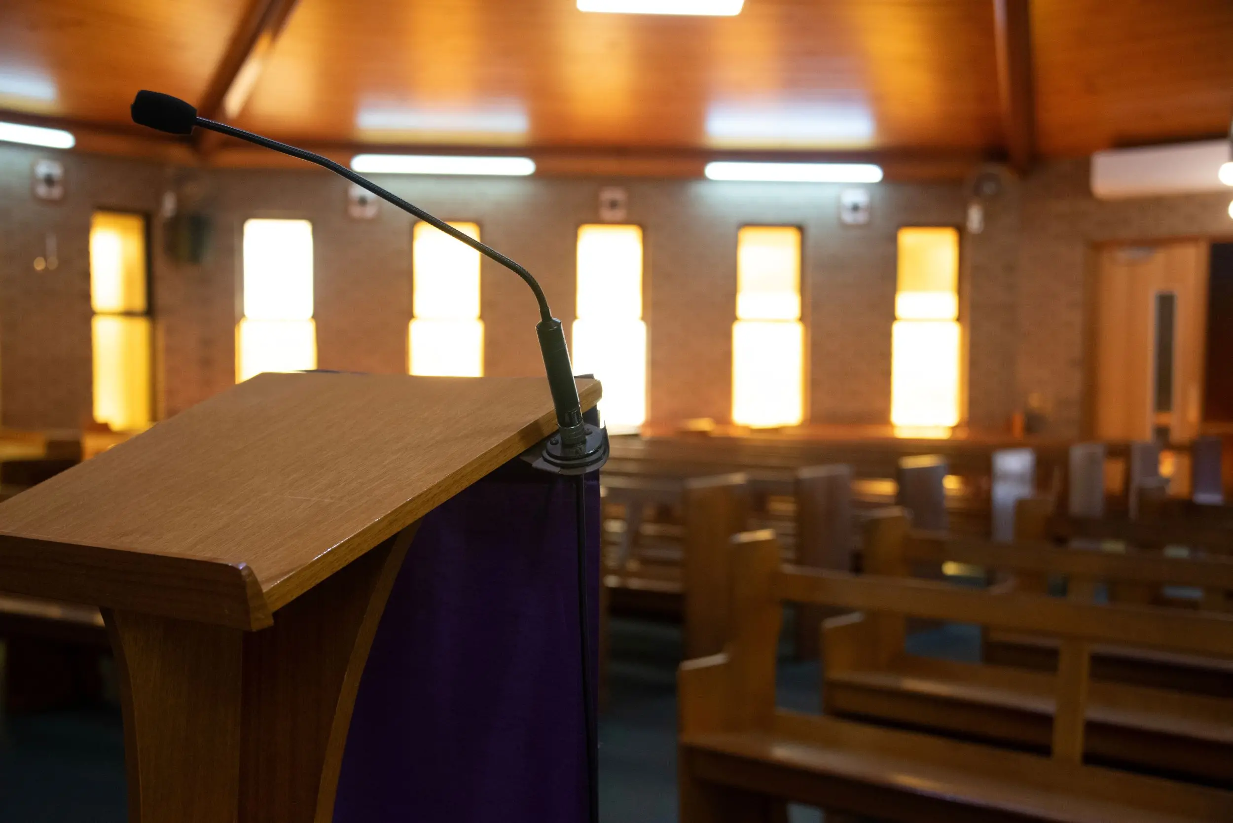 Um púlpito vazio com microfone em destaque, em um ambiente de auditório ou igreja com bancos de madeira.