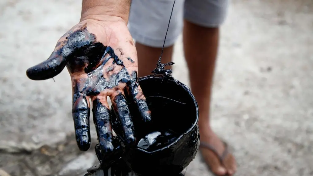 Mão direita suja de um líquido preto e viscoso, parecendo um óleo.