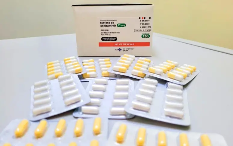 Caixa do medicamento Fosfato de Oseltamivir 75 mg e múltiplos blisters com cápsulas brancas e amarelas, dispostos sobre uma superfície clara.