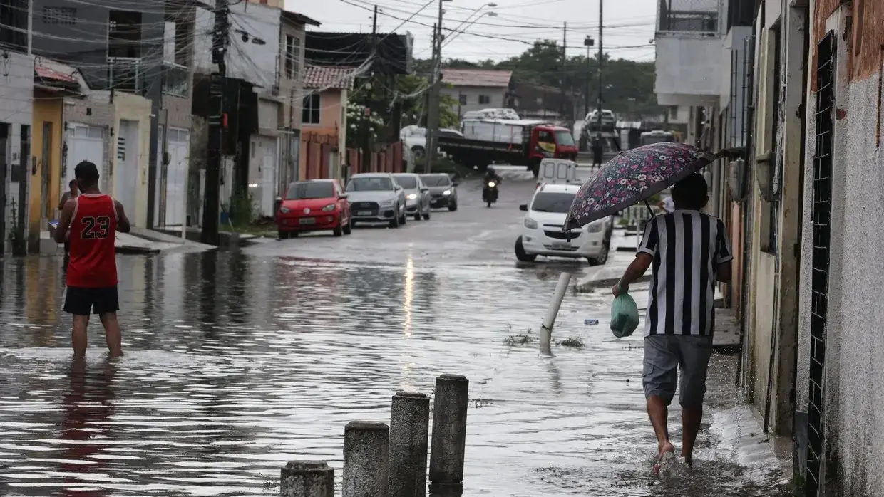 Foto de moradores de Fortaleza em dia de chuva. Imagem mostra rua alagada.
