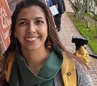 Vitória é uma jovem branca de cabelo liso comprido. Na foto, ela usa casaco cinza com camisa verde de gola alta.