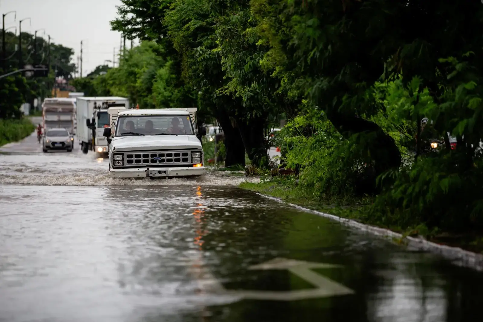 foto de rua alagada e carros e caminhões tentando fazer a travessia.