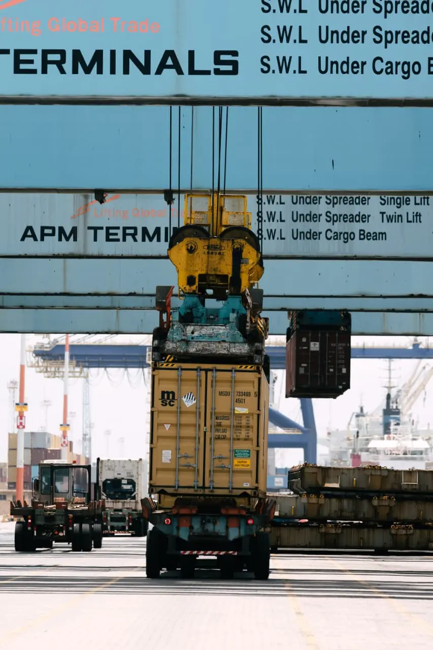 Grua em porto faz transporte de container até a carroceria de um caminhão.