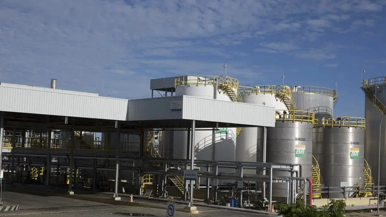 Usina industrial de biodiesel de Quixadá com grandes tanques metálicos cilíndricos, estruturas de tubulação e passarelas amarelas, sob céu parcialmente nublado.