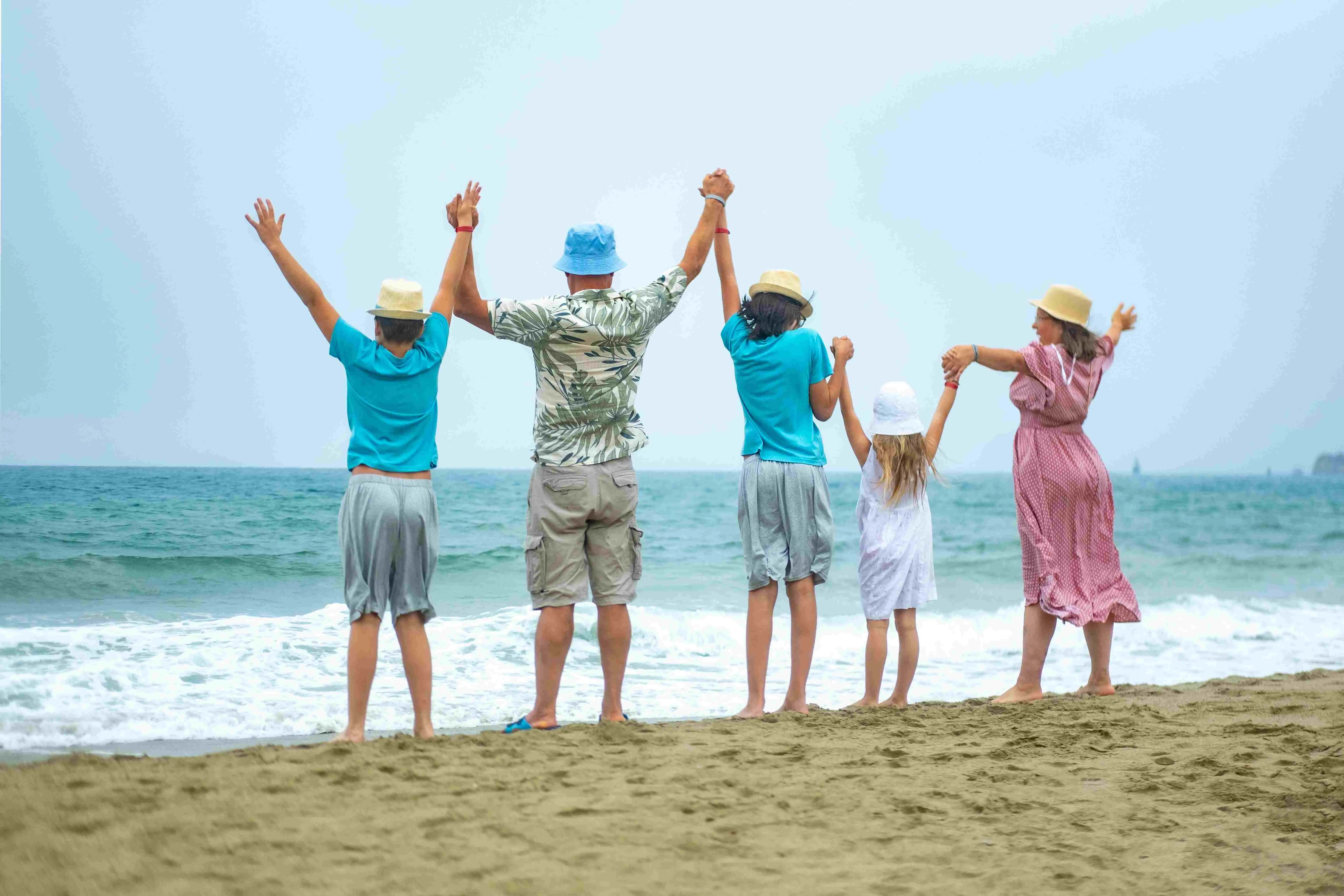 Família grande feliz em pé na praia de areia, olhando para as ondas do oceano juntos, pai com mãe e filhos observando as ondas.