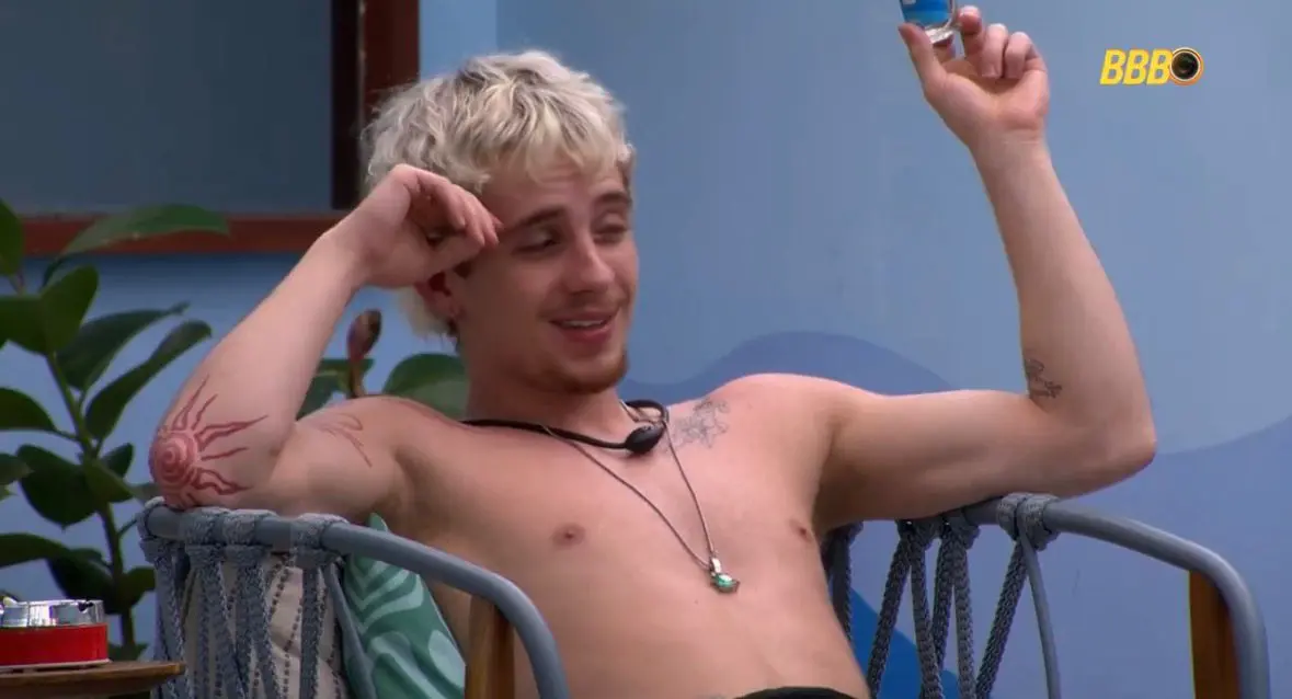 Juliano Floss é um jovem branco e loiro de barba rala. Na foto, ele está sem camisa dialogando.