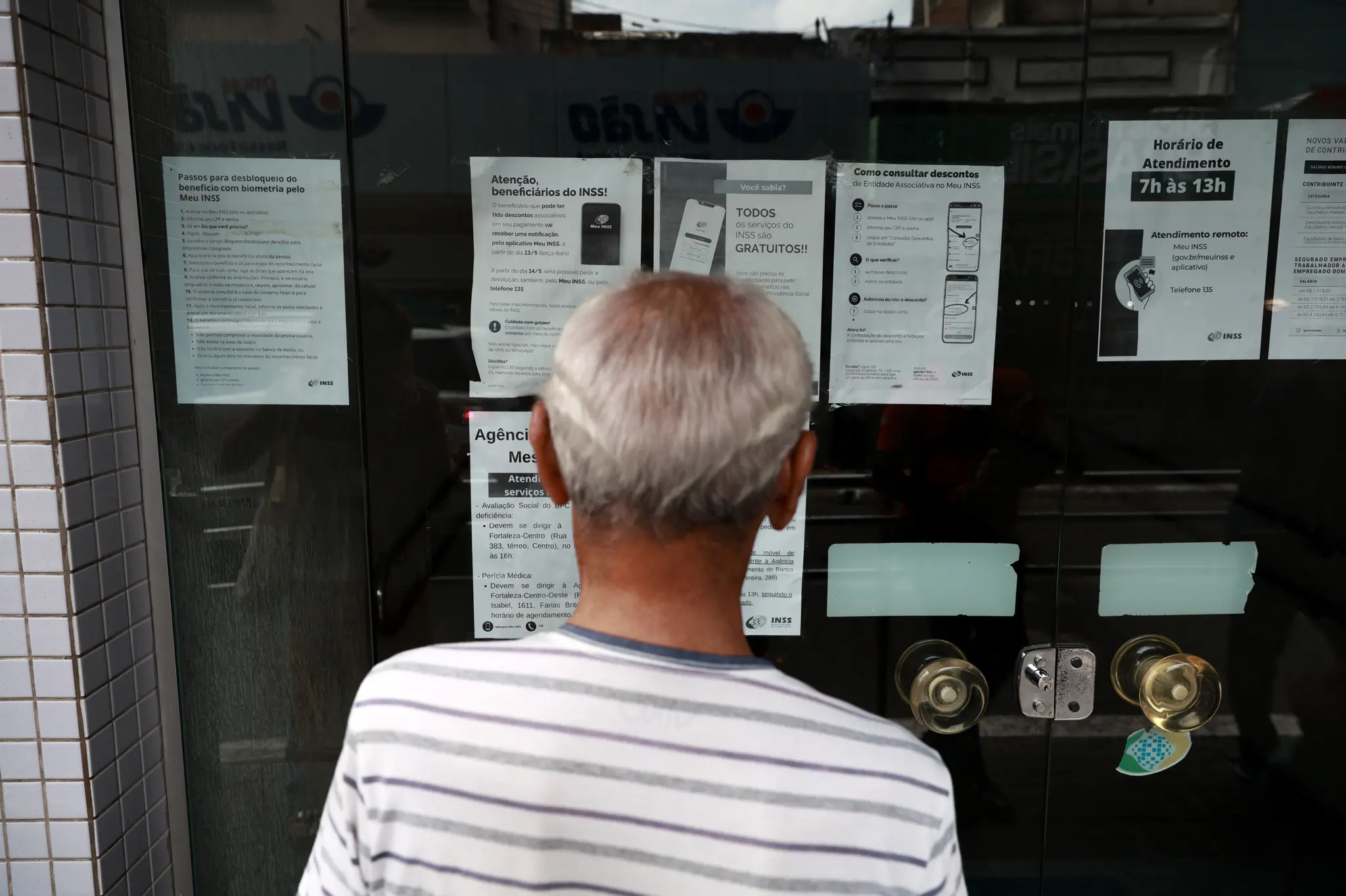 Homem idoso à frente do INSS lendo cartazes.