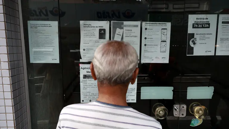 Homem idoso à frente do INSS lendo cartazes.
