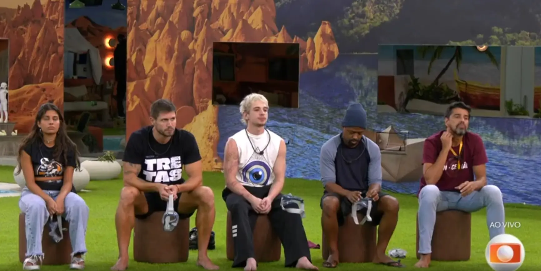 Cinco participantes do reality show BBB 26 estão sentados lado a lado em bancos cilíndricos marrons sobre um gramado artificial. Da esquerda para a direita: uma mulher de camiseta preta e calça jeans clara; um homem de camiseta preta com a palavra 