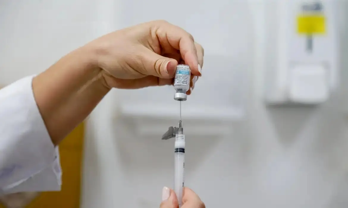 Profissional de saúde preparando uma vacina com seringa para vacinação em ambiente clínico.