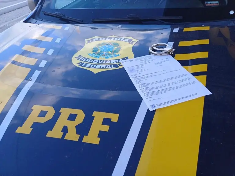 Capô de viatura da Polícia Rodoviária Federal com documento oficial e algemas sobre a superfície.