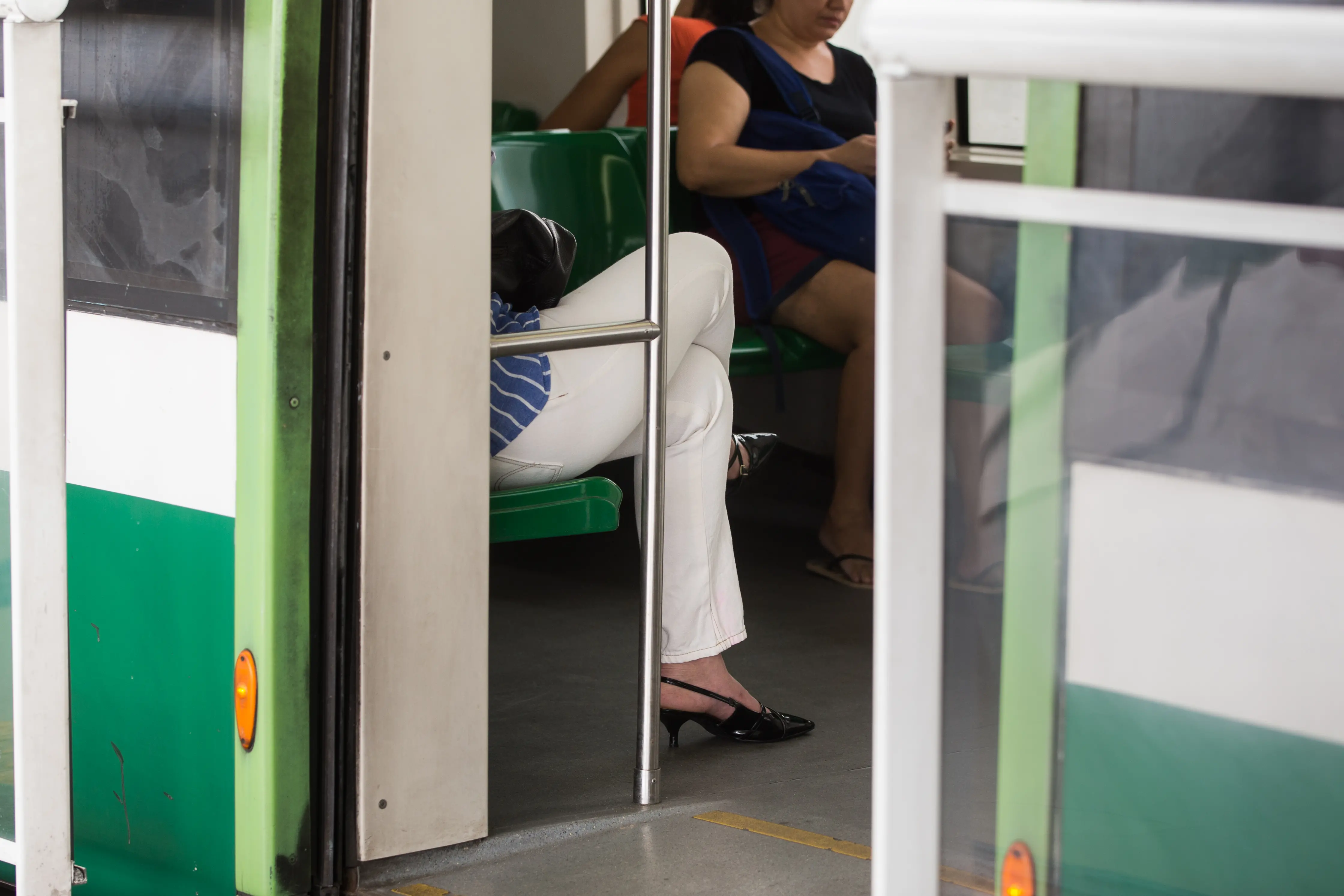 Foto em close das pernas de uma passageira sentada no metrô de Fortaleza; ao fundo, outra pessoa utiliza o transporte.