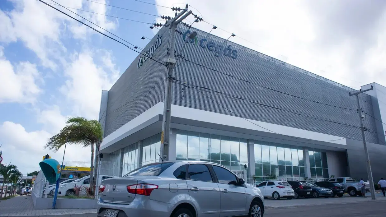 Fachada do prédio da Cegás, com estrutura moderna de vidro e metal, sob céu azul.